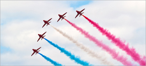 Photo of an air show: five planes releasing trails of coloured smoke in the sky