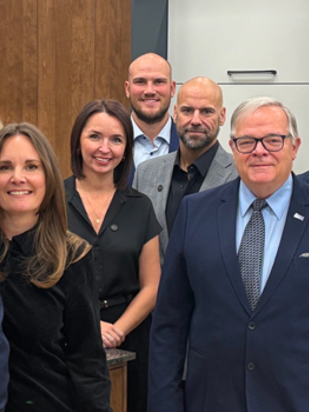 Groupe de personnes debout dans un espace intérieur aménagé, comprenant des armoires et un comptoir, posant pour une photo de groupe.