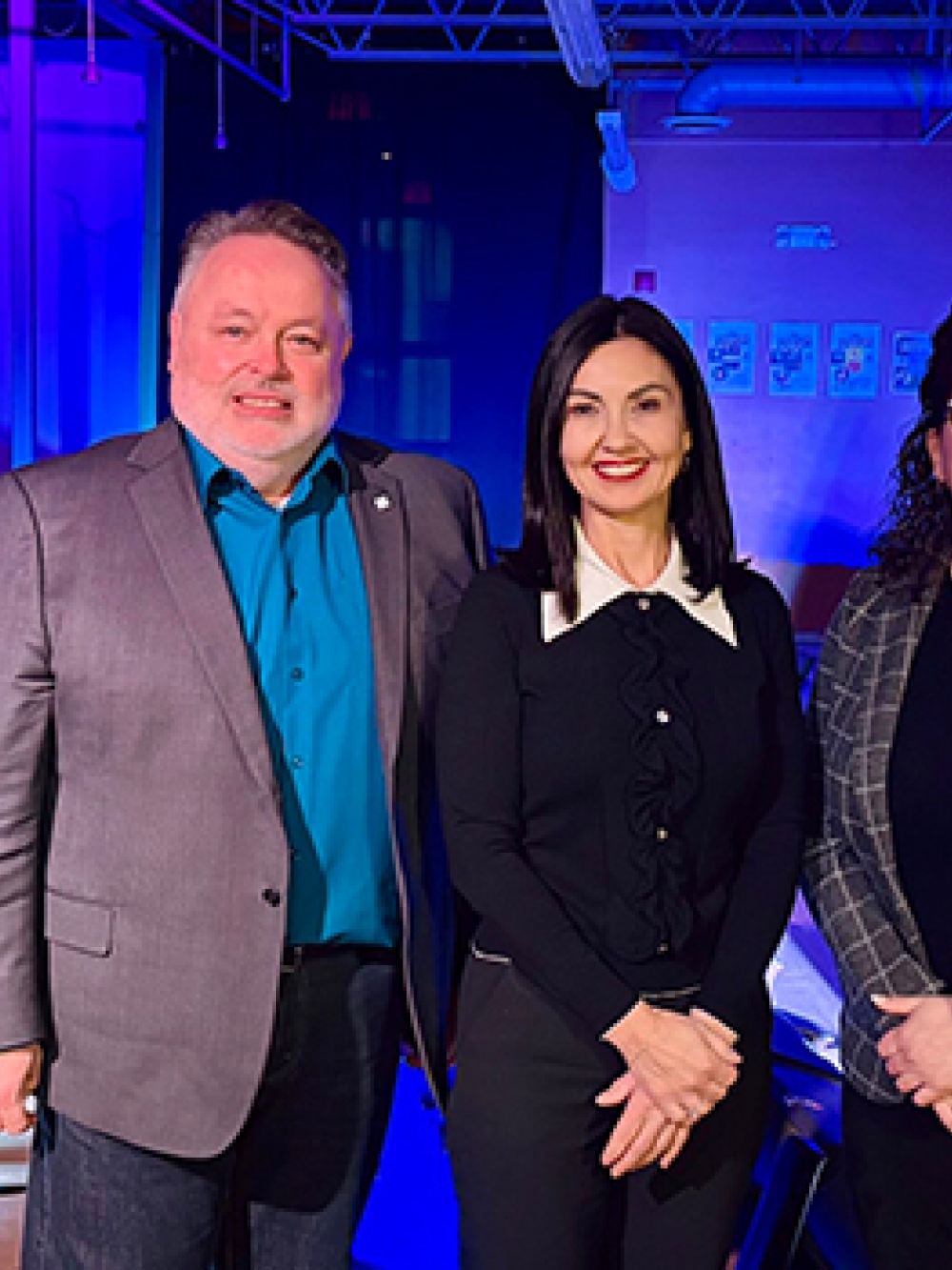 Groupe de cinq personnes posant dans une salle éclairée en bleu, avec un drapeau du Québec et des affiches visibles en arrière‑plan.