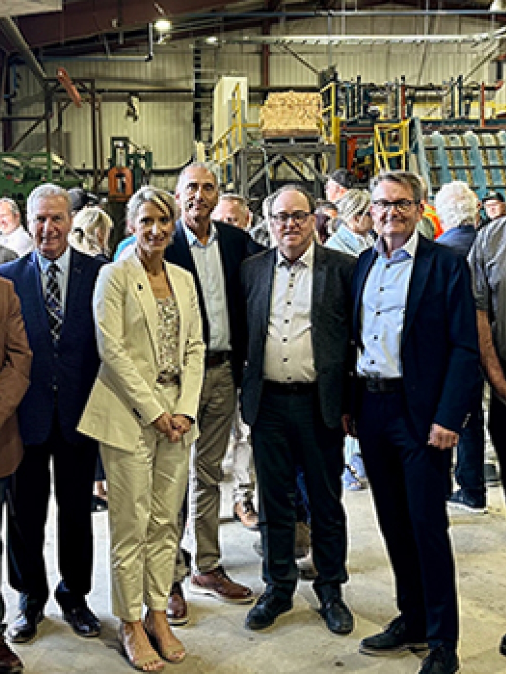 Groupe de personnes debout à l’intérieur d’une scierie, entourées de machines industrielles et d’équipements de production de bois.