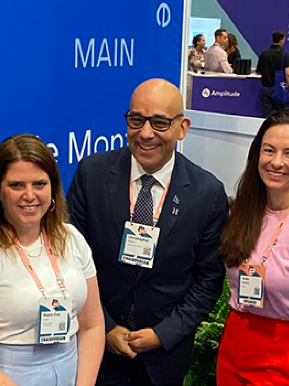 Cinq personnes debout à l’intérieur lors d’un événement professionnel, portant des badges autour du cou, devant un panneau bleu avec le mot « MAIN ».
