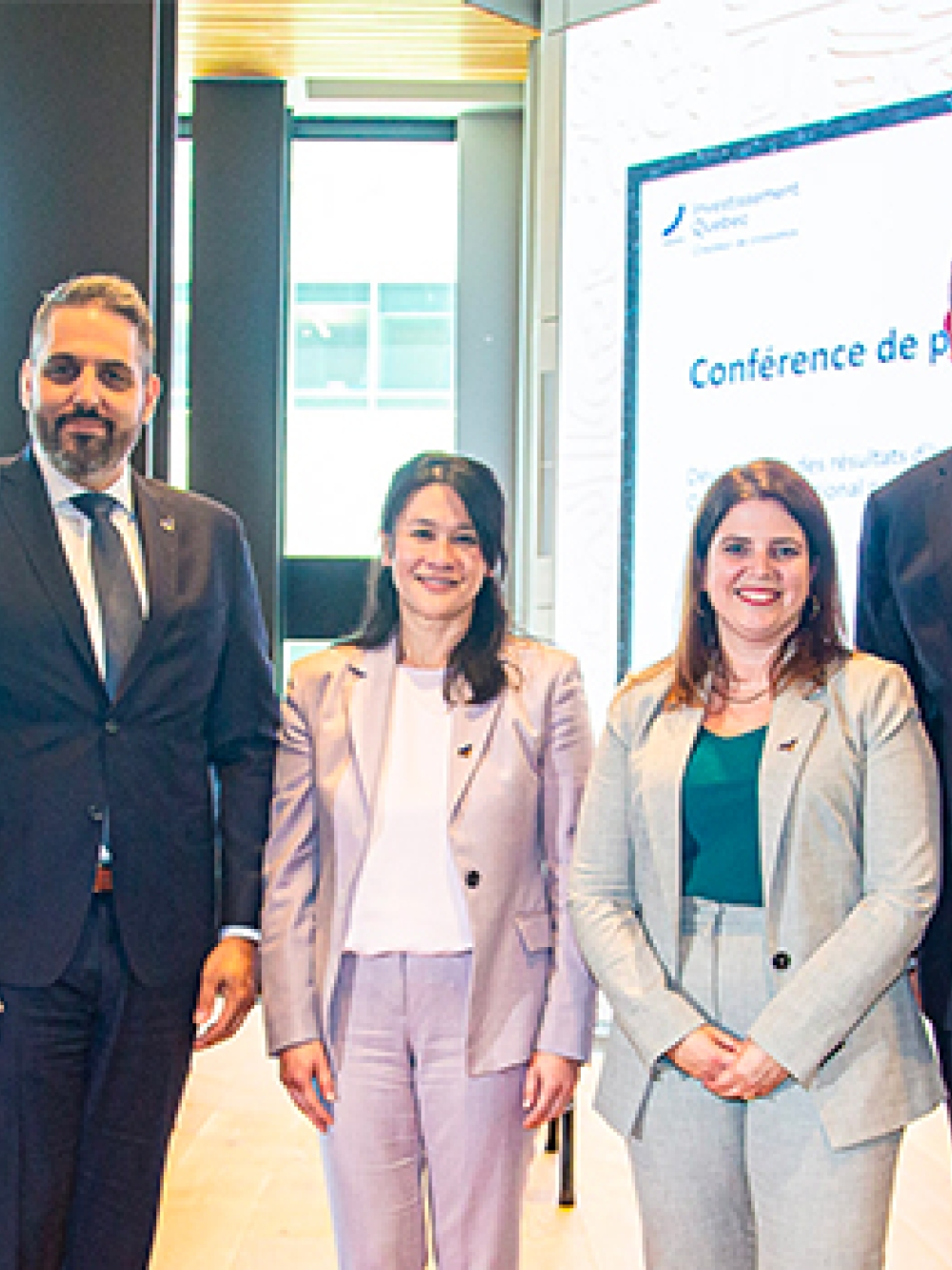 Groupe de personnes posant devant une scène lors d’une conférence de presse, avec un écran de présentation et un drapeau du Québec en arrière‑plan.