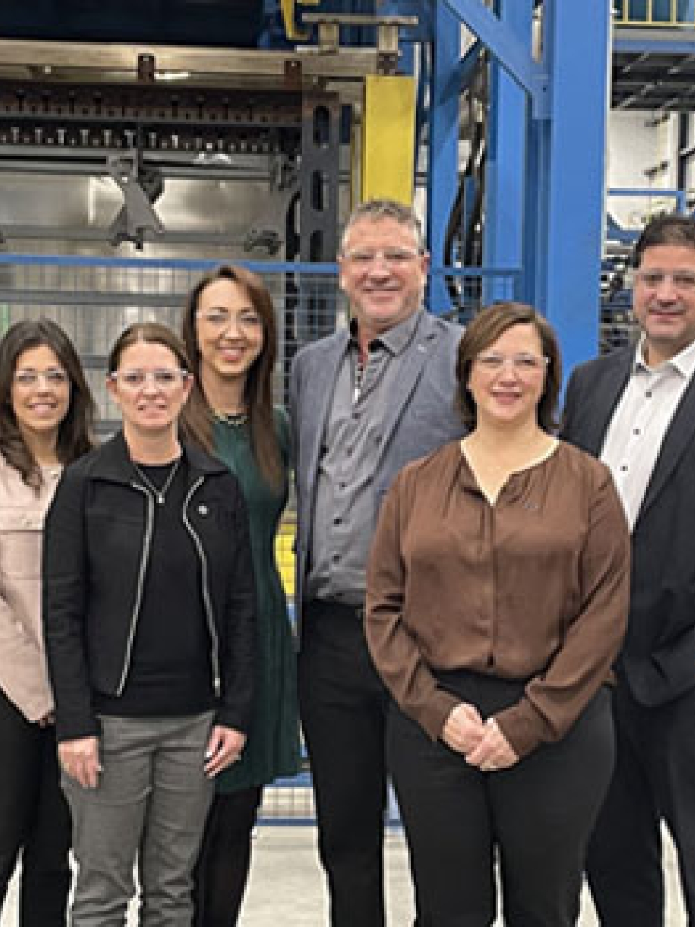 Groupe de personnes debout dans une usine devant de grands équipements industriels bleus et jaunes, posant pour une photo officielle.