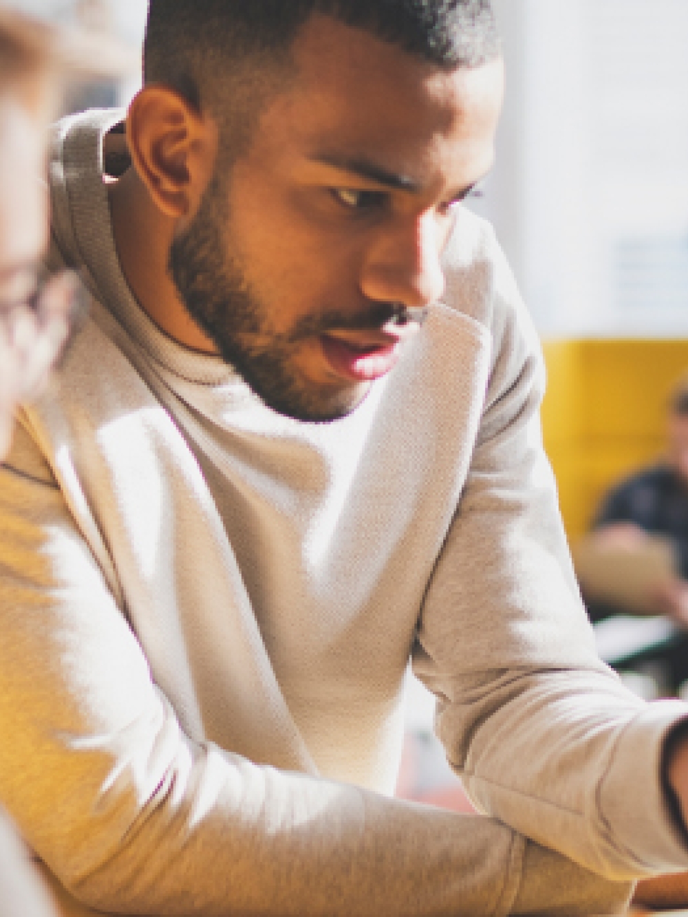 Personne pointant un écran d’ordinateur dans un environnement de bureau moderne, avec d’autres personnes en arrière-plan.