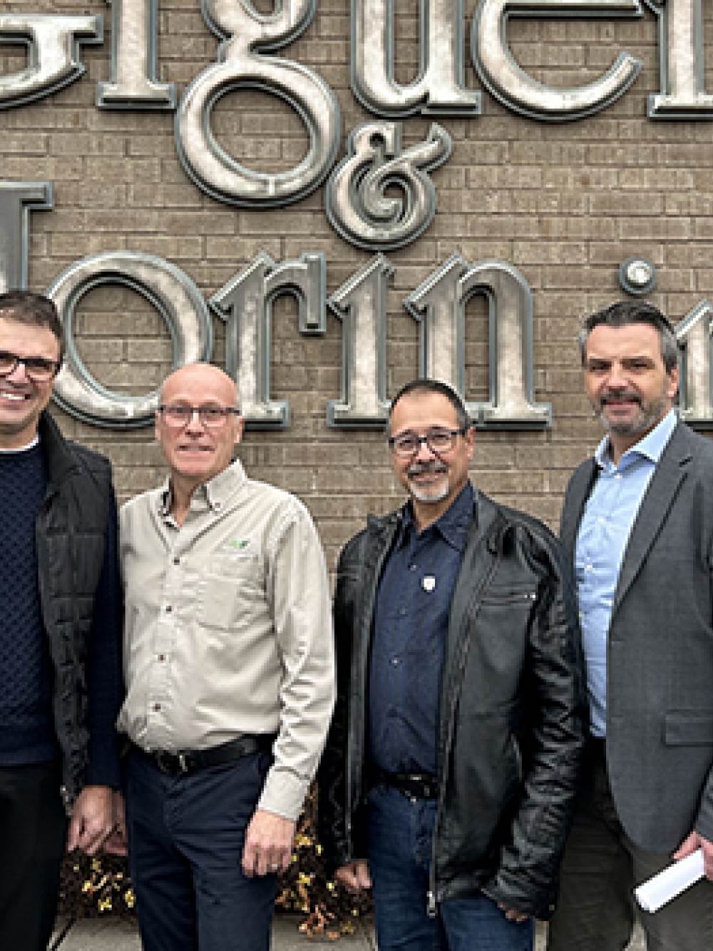 Groupe de personnes debout devant la façade en brique de l’entreprise Giguère & Morin inc., posant pour une photo à l’extérieur du bâtiment.