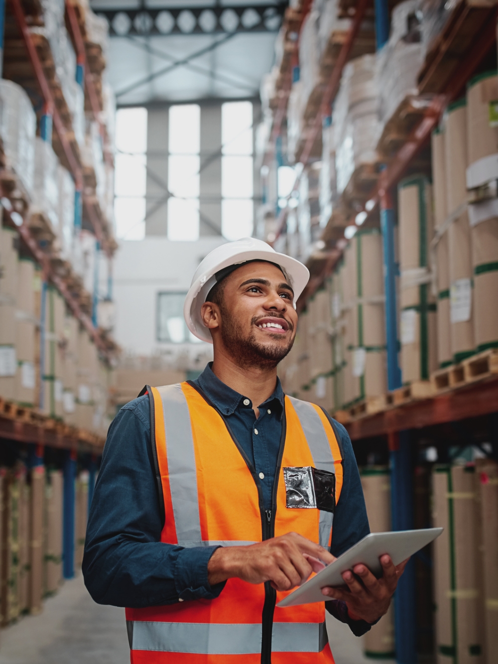 Un travailleur souriant dans un entrepôt portant un dossard orange