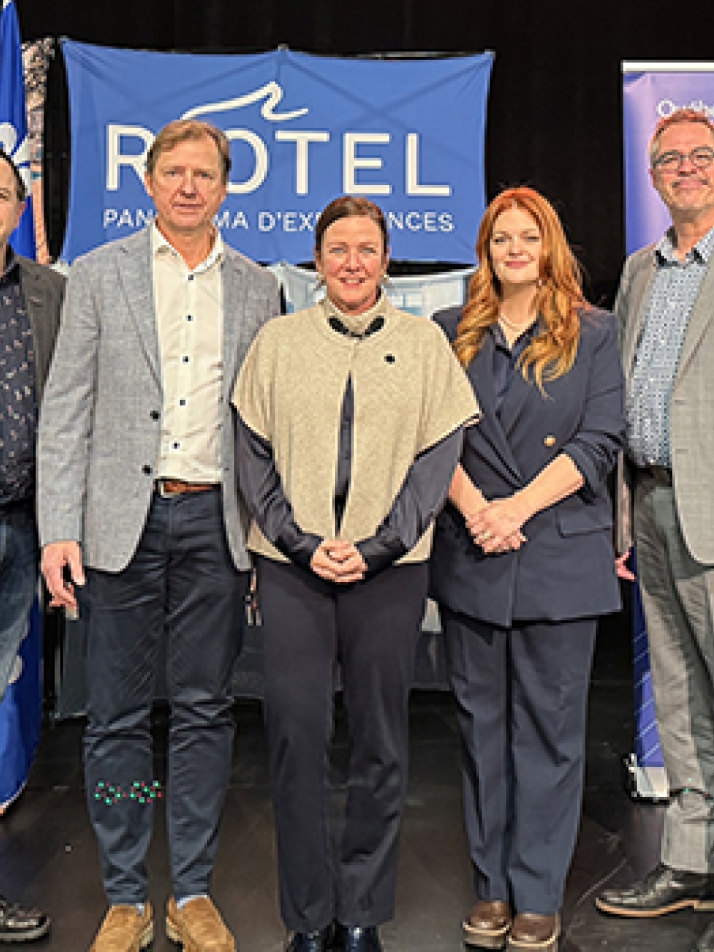 Groupe de personnes posant sur une scène devant des bannières du Riôtel et d’Investissement Québec lors d’un événement officiel.